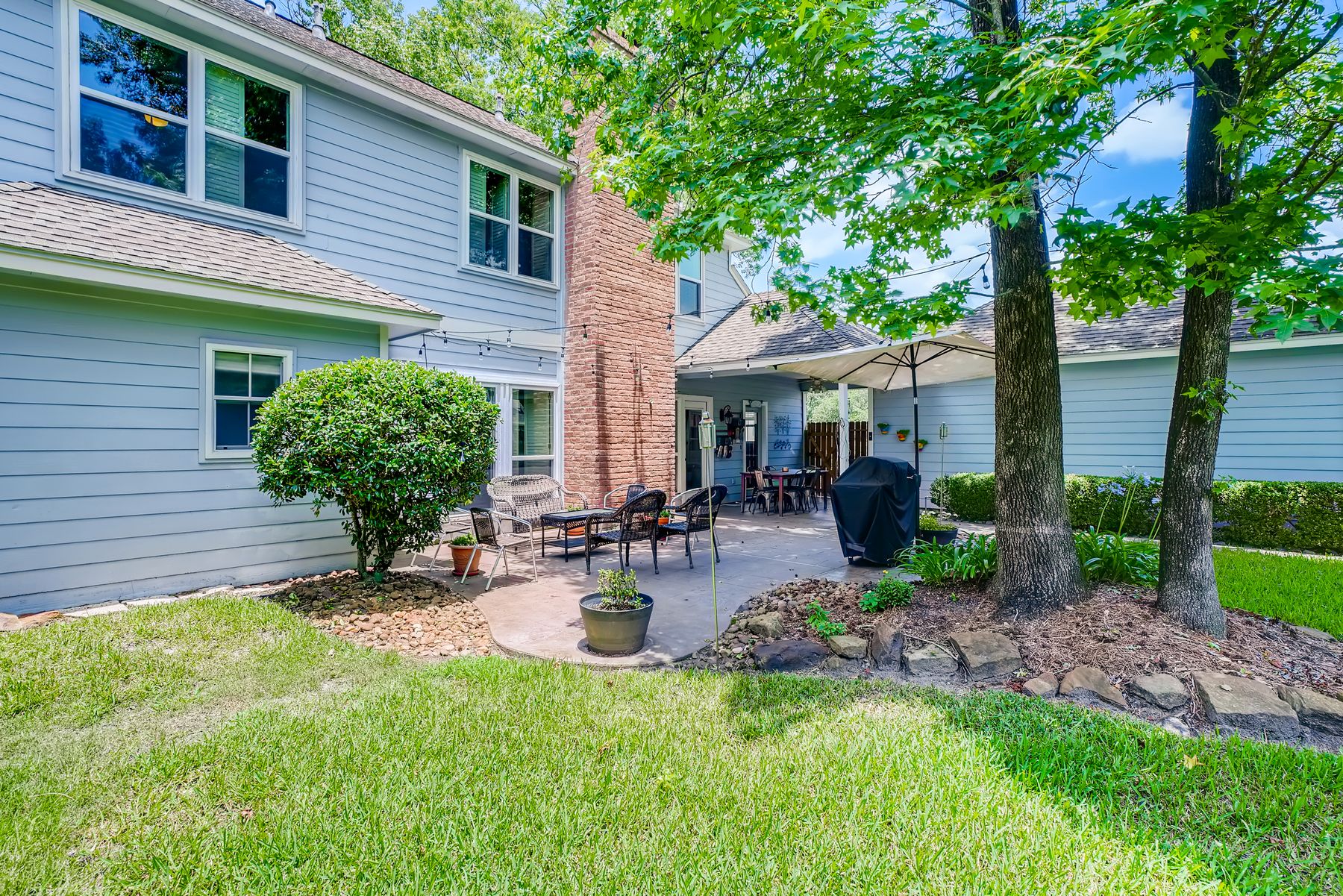 Finished backyard with a clean lawn, patio, trees, and trimmed shrubs